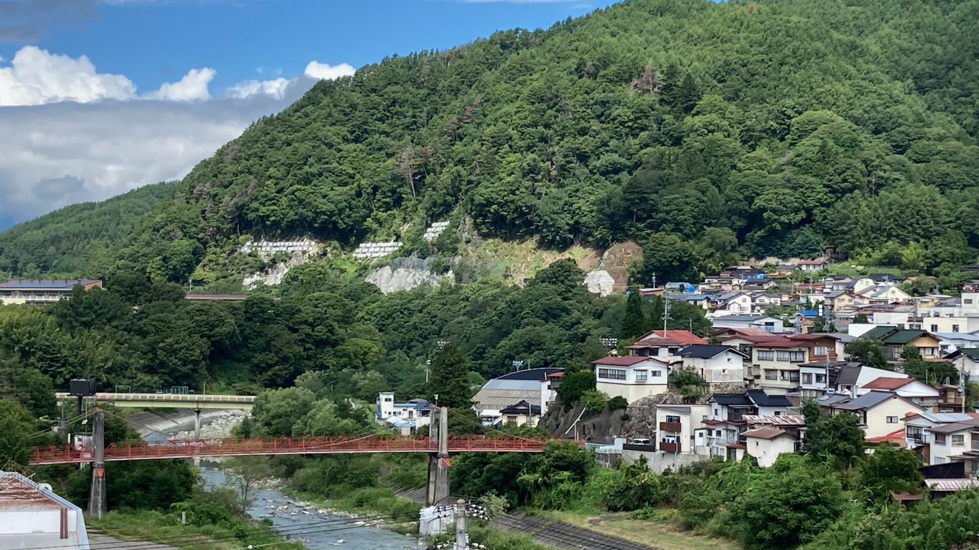 夏の高遠を流れる川と赤い橋、山の斜面に広がる町並み